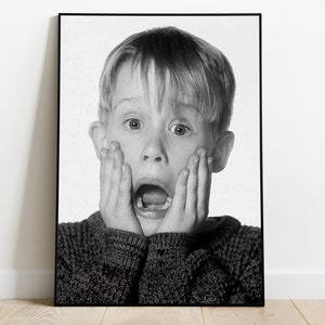 Peut inclure: Photographie en noir et blanc d'un jeune garçon avec une expression surprise, ses mains couvrant son visage. Il porte un pull foncé.