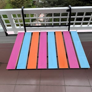 Puede incluir: Una mesa plegable de madera colorida con un marco de metal negro. La mesa est&aacute; pintada en rayas de color rosa, naranja y azul.