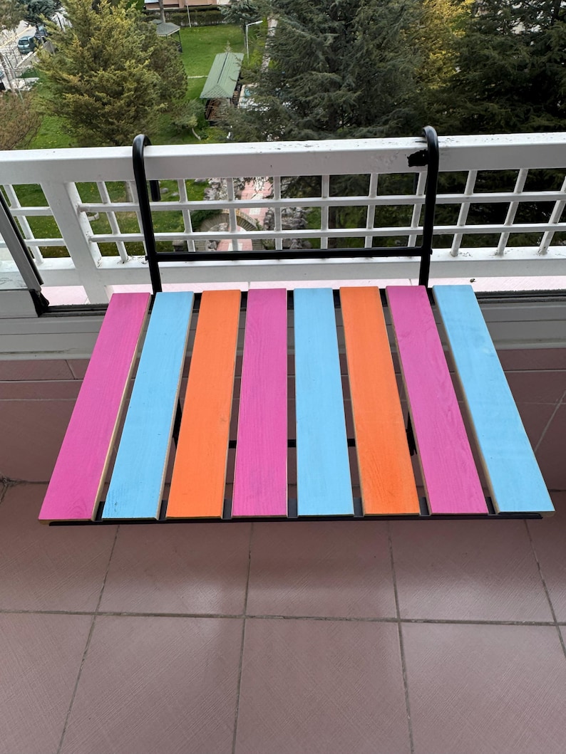 Puede incluir: Una mesa plegable de madera colorida con un marco de metal negro. La mesa est&aacute; pintada en rayas de color rosa, naranja y azul.