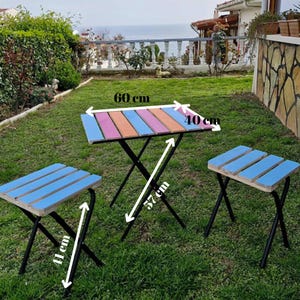 May include: A colorful wooden table and two matching chairs with black metal legs. The table measures 60 cm by 40 cm and is 57 cm tall. The chairs are 41 cm tall.