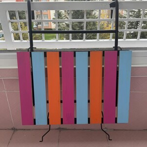 May include: A colorful folding table with a black metal frame. The table is made of wood and has alternating stripes of pink, orange, and blue.