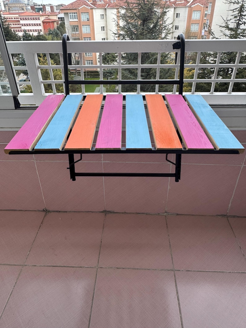May include: A colorful folding table with a black metal frame. The table top is made of wood painted in alternating stripes of pink, blue, and orange.