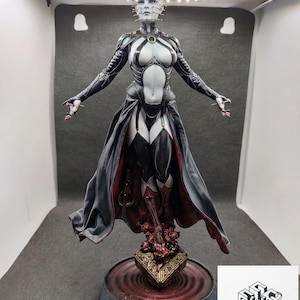 Può includere: Una statuetta dettagliata di una figura umanoide pallida con spilli che sporgono dalla testa, che indossa un abito nero e grigio scuro con un lungo mantello fluente, posizionata su una base con un puzzle box dorato ed elementi rossi.