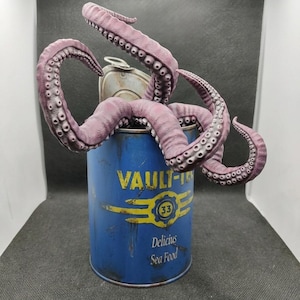 Può includere: Una lattina di metallo blu con la scritta "VAULT-TEC 33 Delicious Sea Food" presenta un polpo viola che emerge dalla parte superiore. La lattina ha un aspetto invecchiato e usurato, che suggerisce un tema vintage o post-apocalittico.
