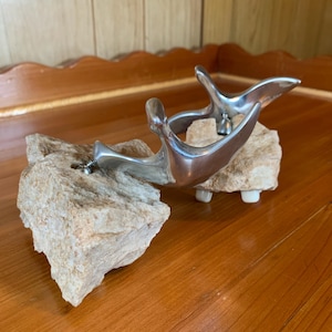 May include: Two silver spurs mounted on rough, light brown rocks. The spurs are made of metal and have a unique, curved design.