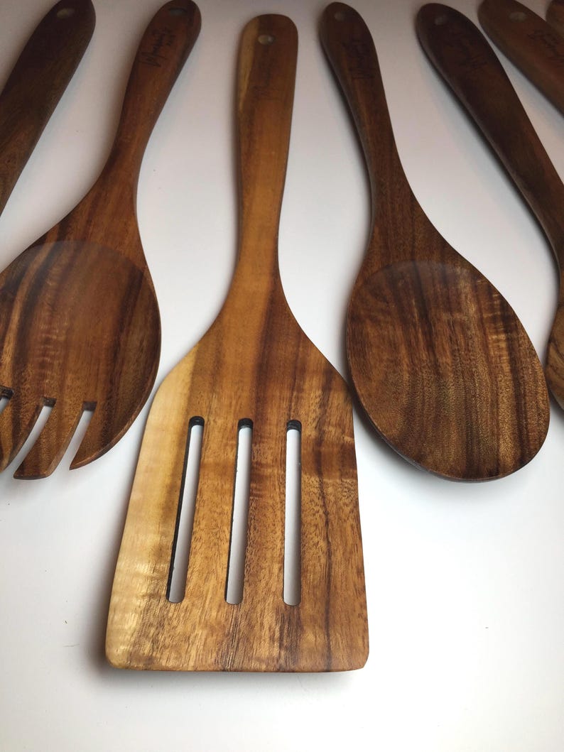 Op de afbeelding: Een verzameling houten keukengerei, waaronder een sleufspatel, lepel en vork. Het keukengerei is gemaakt van een rijk, donkerbruin hout met zichtbare nerfpatronen. De handvatten zijn lang en slank, en het algehele ontwerp is eenvoudig en functioneel.