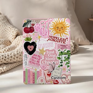 Pode incluir: Uma capa rosa para tablet coberta de autocolantes com um tema romântico. Os autocolantes incluem cerejas, dados, um sol e o texto "Hopeless Romantic". Outros autocolantes dizem "Buy Me Books & Tell Me I'm Pretty" e "Just One More Chapter."