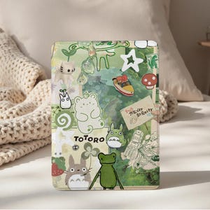 May include: A green and white decorative case featuring various cartoon characters and the word "TOTORO". The case has a collage design with images of a cat, bear, frog, and other whimsical elements.