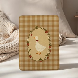 May include: A rectangular case with a tan gingham pattern. The center features an oval illustration of a white goose wearing a red bow, surrounded by a wreath of strawberries and flowers. The case is likely for a tablet or similar device.