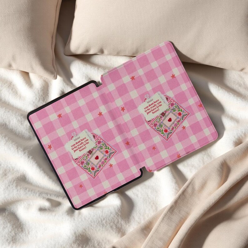 May include: Tablet case with a pink and white gingham design and a black border. It has two embroidered patches with flowers, a heart, and the text "You don't have to be ready, you just have to be brave!"