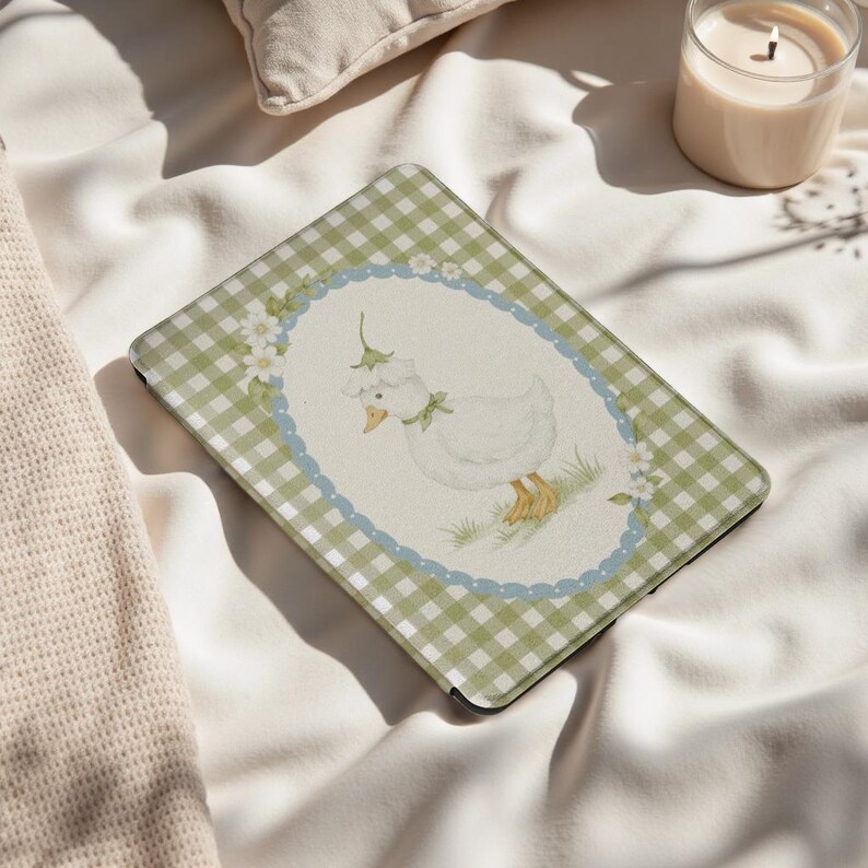 May include: An iPad case featuring a whimsical illustration of a white goose wearing a bonnet and a green bow, set against a cream background. The case has a green and white gingham pattern border with a blue scalloped edge.