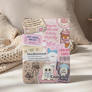 Könnte beinhalten: Eine dekorative Buchhülle mit einer Collage aus Aufklebern in Rosa- und Beigetönen. Die Aufkleber zeigen Sätze wie "booktrovert", "Anti-Social Book Club" und "buy me books and tell me I'm pretty". Ein Cartoon-Geist, der ein Buch liest, ist ebenfalls zu sehen.