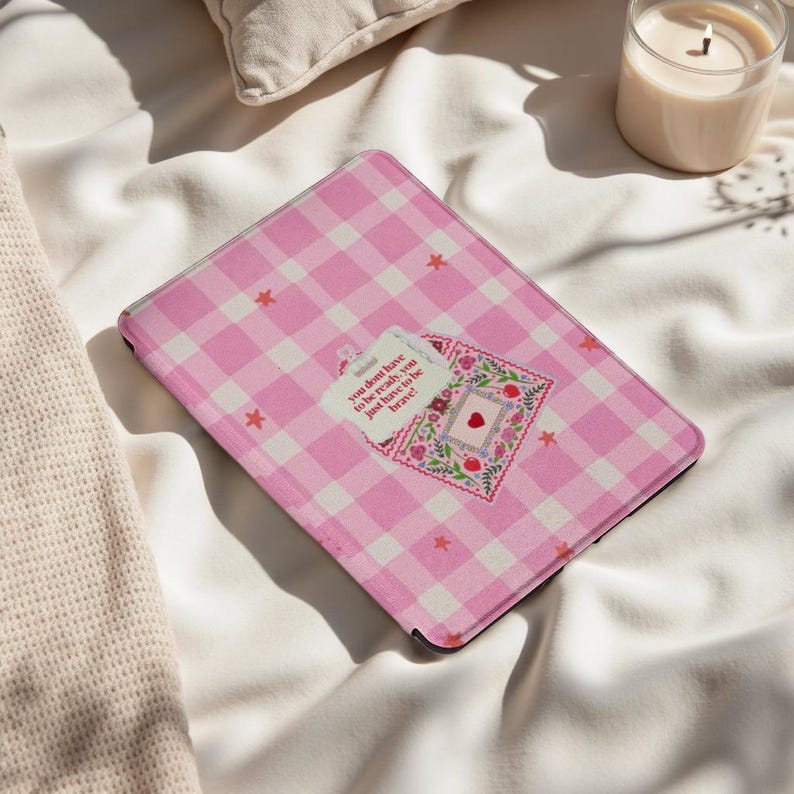 May include: Tablet case in a pink and white gingham pattern, featuring a floral and heart motif. The case displays the text "you don't have to be ready, you just have to be brave!". Small red stars are scattered across the case.