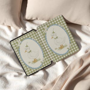 May include: A green and white gingham pattern tablet case with a whimsical illustration of a white duck wearing a bonnet. The duck is inside a blue oval frame with floral accents. The case is open, revealing the interior.