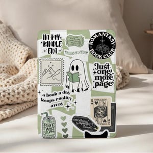 Puede incluir: Una funda Kindle con un patrón verde y blanco, adornada con pegatinas. Las pegatinas incluyen un fantasma leyendo un libro, el texto "In My Kindle Era" y "Romantasy Book Club". Otras pegatinas presentan una escena de montaña y naipes.
