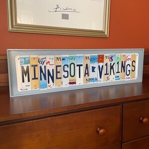 May include: A framed wall art piece made from vintage number plates spelling out "Minnesota Vikings".