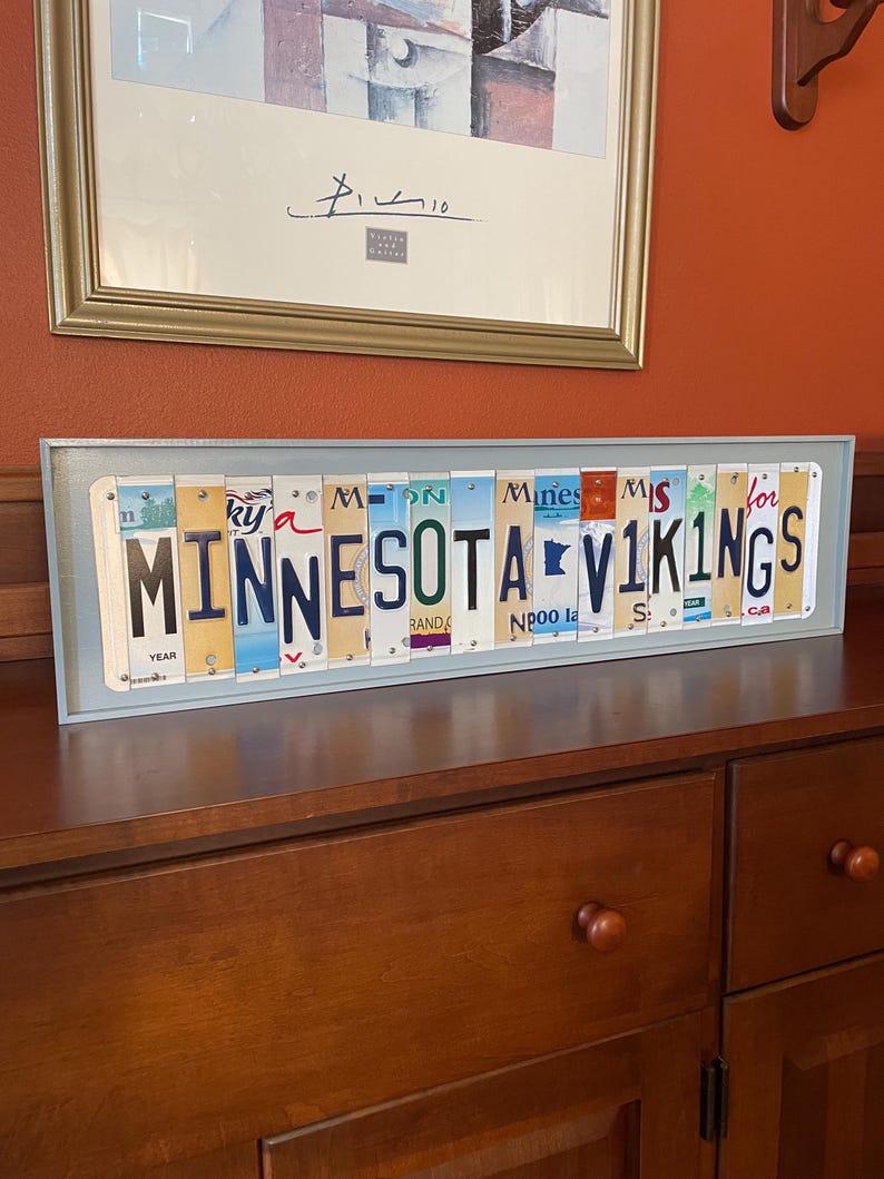 May include: A framed wall art piece made from vintage number plates spelling out "Minnesota Vikings".