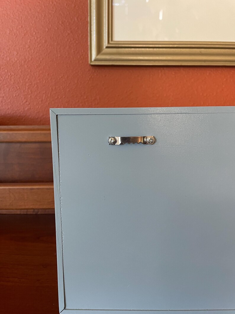 May include: A light blue wooden box with a silver metal handle. The box is closed and has a smooth surface.