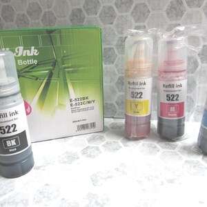 Op de afbeelding: Een verzameling navulinktflesjes en een groene doos. De flesjes zijn gelabeld met "Refill ink 522" met de kleuren zwart, geel, magenta en cyaan. De doos is gelabeld met "Ink Bottle" en "E-522BK E-522C/M/Y".