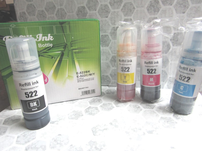 Op de afbeelding: Een verzameling navulinktflesjes en een groene doos. De flesjes zijn gelabeld met "Refill ink 522" met de kleuren zwart, geel, magenta en cyaan. De doos is gelabeld met "Ink Bottle" en "E-522BK E-522C/M/Y".