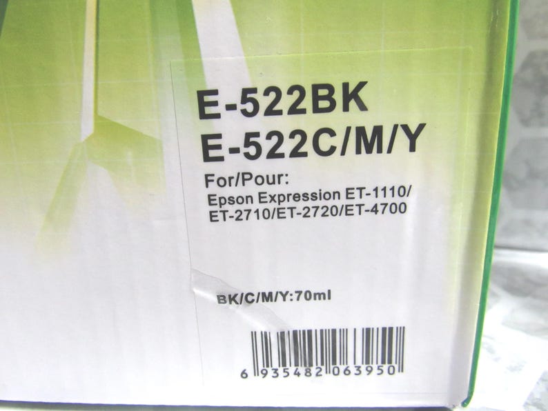 Op de afbeelding: Close-up van een doos met de tekst "E-522BK E-522C/M/Y" en "For/Pour: Epson Expression ET-1110/ ET-2710/ET-2720/ET-4700". De doos geeft ook "BK/C/M/Y:70ml" aan en heeft een barcode.