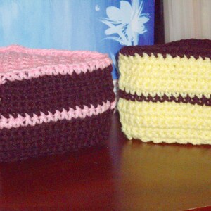 Pode incluir: Duas almofadas de crochê em forma de bolo. Uma é rosa e marrom, a outra é amarela e marrom.