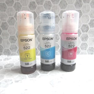 Op de afbeelding: Drie Epson inktflessen, gelabeld met 522, in geel, cyaan en magenta. Elke fles heeft een doorzichtige bovenkant en een zwarte basis. De gele fles is gelabeld met "Y", de cyaan fles is gelabeld met "C", en de magenta fles is gelabeld met "M".