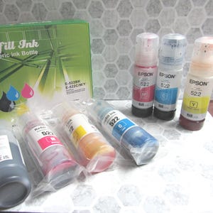 Op de afbeelding: Een verzameling Epson 522 navulinktflessen in verschillende kleuren, waaronder zwart, magenta, cyaan en geel. De flessen worden getoond met een groene doos met het opschrift "Refill Ink" en zijn ontworpen voor algemeen gebruik.