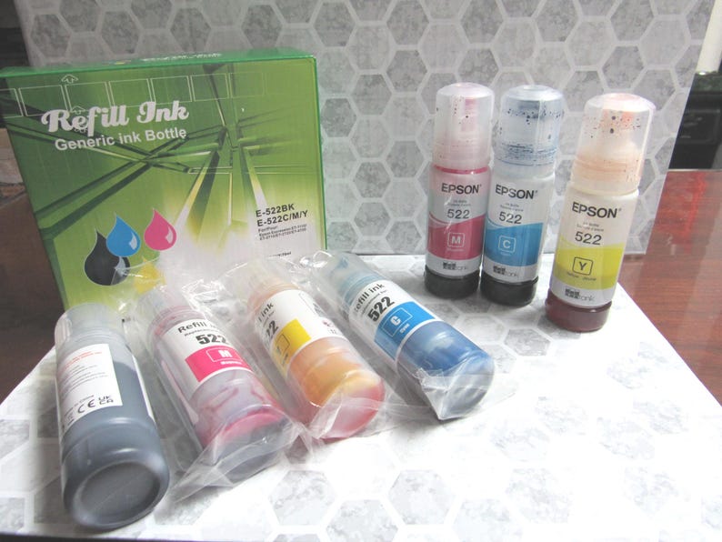 Op de afbeelding: Een verzameling Epson 522 navulinktflessen in verschillende kleuren, waaronder zwart, magenta, cyaan en geel. De flessen worden getoond met een groene doos met het opschrift "Refill Ink" en zijn ontworpen voor algemeen gebruik.