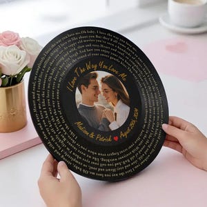 May include: A black vinyl record with a gold inscription that reads "I love the way you love me". The record features a photo of a couple with the names "Madison & Patrick" and the date "August 25th, 2022".