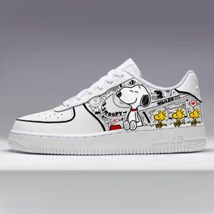 May include: A white sneaker featuring a custom graphic design of the character Snoopy and three yellow Woodstock birds. The illustration includes black outlines, the text SNOOPY and WAHOO, a red collar, a red dog bowl, and a small red heart icon.