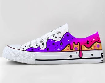 May include: White canvas low-top sneaker with a colorful, artistic design. The design features a purple, orange, and pink dripping pattern on the side, with black dots and stars. The laces are white.