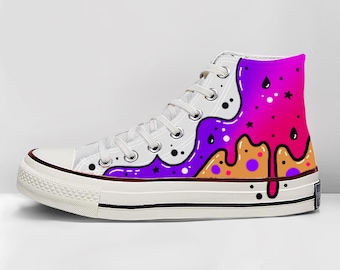 May include: White high-top sneaker with a colorful design. The design features a dripping pattern in shades of purple, orange, and pink, with black dots and stars. The sneaker has white laces and a white sole with a black stripe.