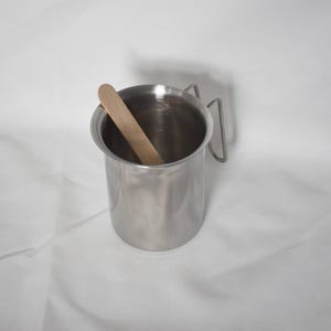 K&ouml;nnte beinhalten: Eine Tasse aus Edelstahl mit einem Griff und einem Holzr&uuml;hrstab im Inneren.
