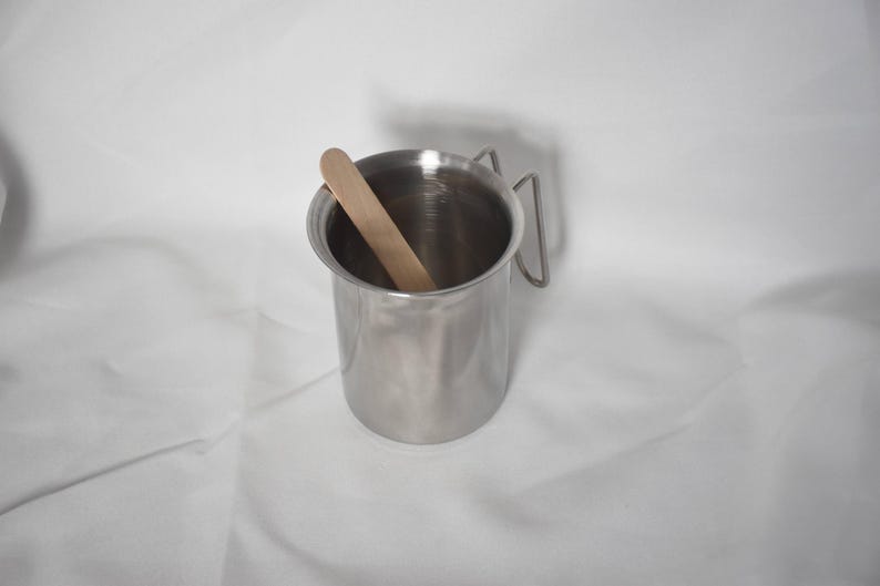 K&ouml;nnte beinhalten: Eine Tasse aus Edelstahl mit einem Griff und einem Holzr&uuml;hrstab im Inneren.
