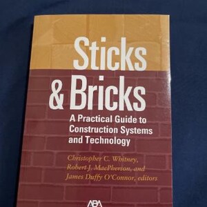 May include: A book titled "Sticks & Bricks" with a brick-patterned cover. The top portion is tan, and the bottom is red brick. The title is in large white letters. The book is a practical guide to construction systems and technology.