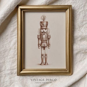 Puede incluir: Una impresión enmarcada en tonos sepia de un soldado cascanueces. La obra de arte está en un marco dorado y presenta el texto "VINTAGE DISCO Curated Timeless Art" en la parte inferior. El cascanueces está detallado con sombrero, bigote y uniforme.