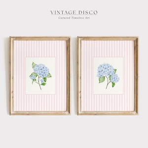 May include: Two framed floral prints featuring light blue hydrangea blooms with green leaves. The artwork is set against a pink and white striped background, encased in a light brown wooden frame. The text "VINTAGE DISCO" and "Curated Timeless Art" are at the top.