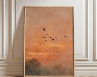 May include: A framed art print featuring a sunset scene with birds in flight. The artwork has a warm color palette of orange, peach, and brown. The birds are silhouetted against the sky, and the print is displayed on a wooden floor.