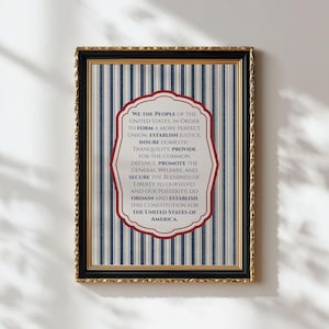 May include: Framed print featuring the text of the U.S. Constitution's Preamble. The text is in a red and white oval shape, set against a blue and white striped background. The frame is black and gold.