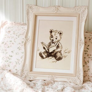 May include: A framed sepia-toned print of a teddy bear reading a book. The ornate, cream-colored frame is set against a backdrop of floral pillows and bedding. The image evokes a sense of nostalgia and comfort, suitable for a nursery or bedroom.