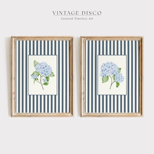 May include: Two framed art prints featuring blue hydrangea watercolor paintings. The frames have a light wood finish and are set against a navy and white striped background. The text "VINTAGE DISCO" and "Curated Timeless Art" is at the top.