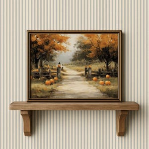 May include: A framed painting of an autumnal scene with a path, pumpkins, and trees. The artwork uses warm colours like orange, brown, and yellow, with a wooden fence and lanterns. The painting is displayed on a wooden shelf, evoking a cozy, seasonal atmosphere.