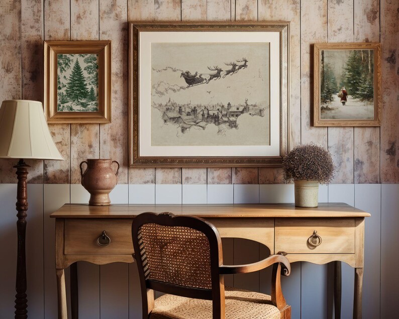 May include: A cozy interior scene featuring a wooden desk with a lamp, vase, and chair. Above the desk are three framed artworks: a Christmas tree print, a Santa sleigh scene, and a winter landscape. The wall has a wood paneling design.