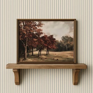 Puede incluir: Una pintura de paisaje otoñal en un marco dorado. La obra representa árboles con hojas rojas y marrones en un campo, con un bosque al fondo. La pintura se exhibe en una estantería de madera.