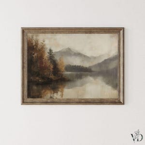 May include: A framed landscape painting depicts a serene lake scene with mountains in the background. The artwork features a muted color palette of browns, greens, and grays, with trees on the left and a reflection in the water.