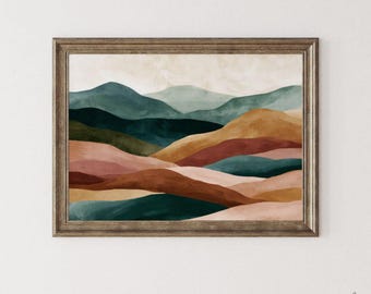 Puede incluir: Una impresión artística enmarcada que representa un paisaje de colinas onduladas en tonos verdes, marrones y rosas. La obra de arte tiene un efecto de acuarela y se encuentra sobre un cielo color crema. El marco es de un tono cálido de madera natural.