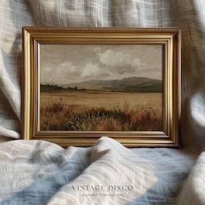 May include: A framed landscape painting with a gold ornate frame. The artwork depicts a field of tall grass in shades of brown and tan, with a mountain range in the background under a cloudy sky. The text "VINTAGE DISCO" and "Curated Timeless Art" is at the bottom.