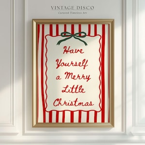 Puede incluir: Un estampado navideño enmarcado con un marco dorado. La obra de arte presenta un fondo crema con rayas verticales rojas y un rectángulo central crema con las palabras "Have Yourself a Merry Little Christmas" en escritura roja. Un lazo verde en la parte superior.