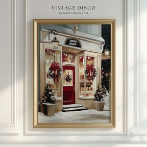 May include: A framed painting of a snow-covered book shop with a red door and Christmas decorations. The shop has a sign that reads "BOOK SHOP". The painting is in a gold frame and is hanging on a white wall.